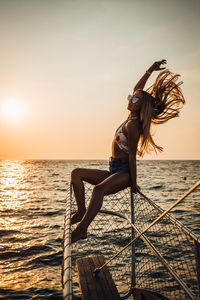 Woman with umbrella on sea against sky during sunset