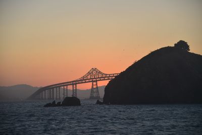 Silhouette bridge over sea against orange sky