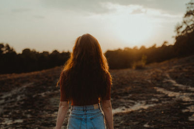 Rear view of woman standing on field against sky during sunset
