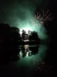 Firework display over lake against sky at night