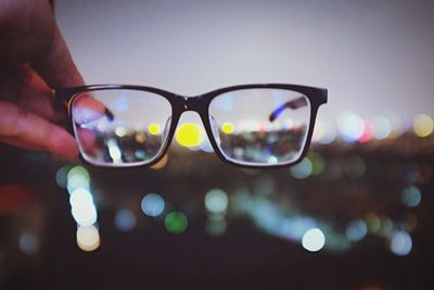 Close-up of hand wearing sunglasses against sky at night