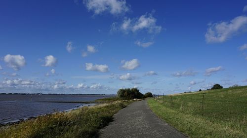 Empty road amidst field against sky