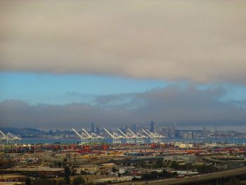 Cranes at harbor against cloudy sky