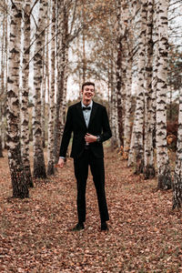 Full length of young man standing amidst trees in forest