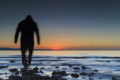 Rear view of silhouette woman standing at beach during sunset