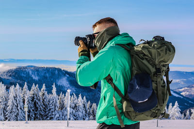 Rear view of man photographing on snow covered mountain