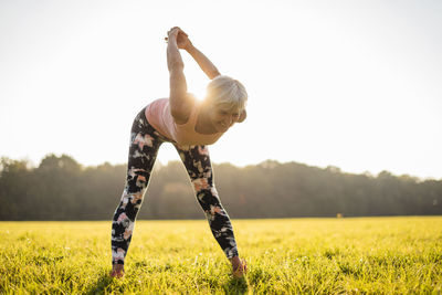 Senior woman stretching on rural meadow at sunset