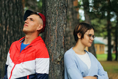 Young man standing by tree trunk