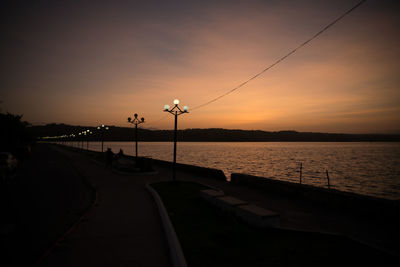 Street by lake against sky during sunset