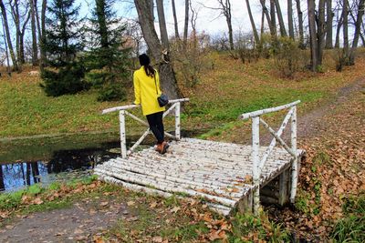 Full length of woman standing on footbridge over stream