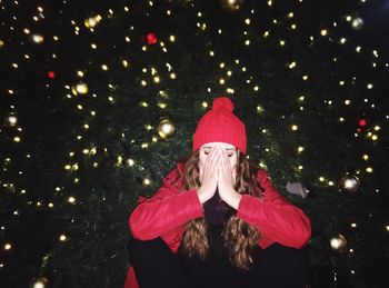 Woman covering face with hands against christmas tree at night