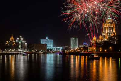 Firework display over river by buildings in city at night