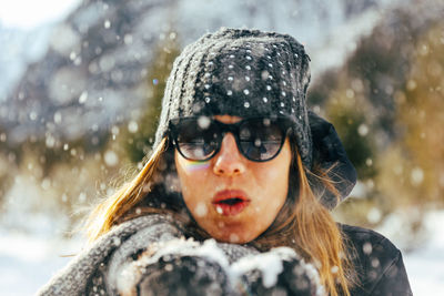 Solo female blowing snow in camera in europe with winter hat and black sunglasses on