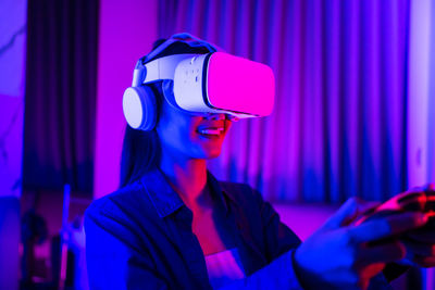 Smiling woman using virtual simulator in illuminated room