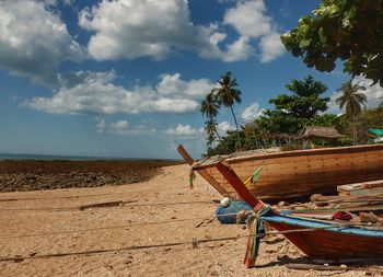 Boats moored at beach against cloudy sky