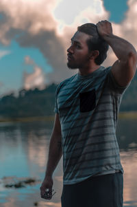 Young man looking away while standing on lake against sky