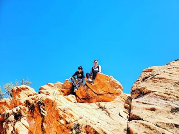 People on rocks by mountain against clear blue sky