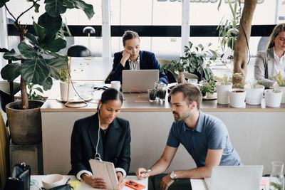 Colleagues discussing while businesswoman working on laptop at office