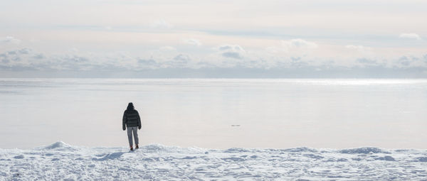 Rear view of man standing at snow covered shore
