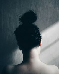 Rear view of shirtless woman with hair bun against wall