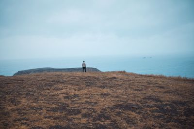 Rear view of man standing on cliff against sky