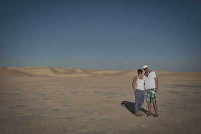 Rear view of people walking on desert against clear sky