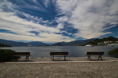 Empty bench by lake against sky