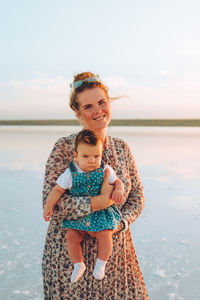 Happy smiling woman with red hair holding her child and walking by the sea