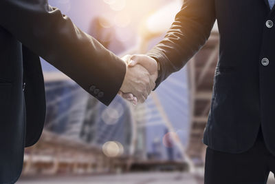 Midsection of colleagues giving handshake while standing outdoors