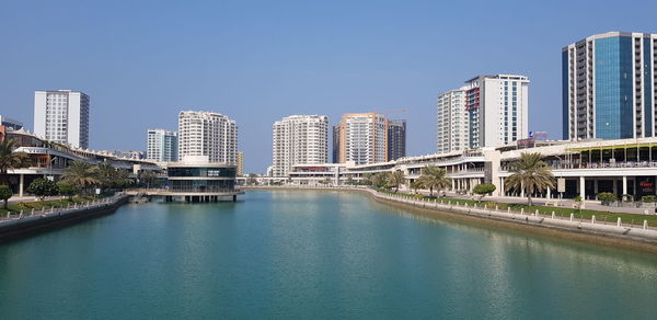 View of modern buildings by canal against clear blue sky