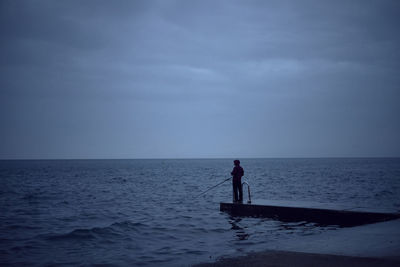Silhouette man standing in sea against sky