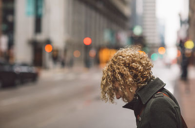 Side view of woman standing on sidewalk in city