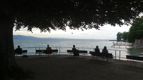 Silhouette people sitting on table by sea against sky