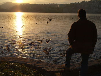 Rear view of silhouette man standing by lake