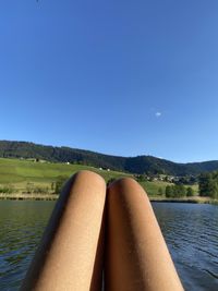 Low section of woman relaxing on water against clear sky