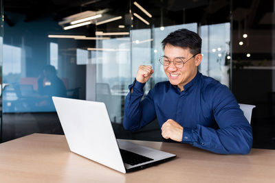 Portrait of young man using laptop at desk in office