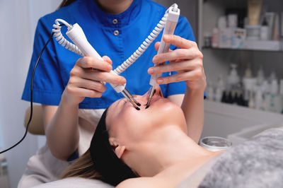 Close-up of a professional cosmetologist's hands touching a woman's cheek with equipment. young