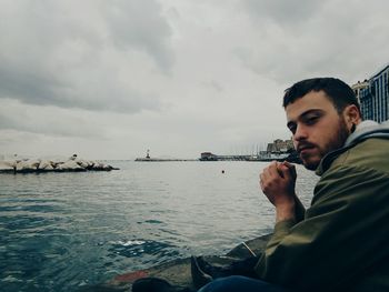 Young man sitting on rock against sea