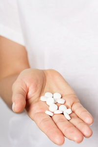 Cropped hand of woman holding pills against white background