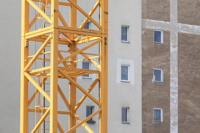 Yellow crane in front of old residential building with illegal windows on a fire protecting wall