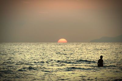 Silhouette man in sea against sky during sunset