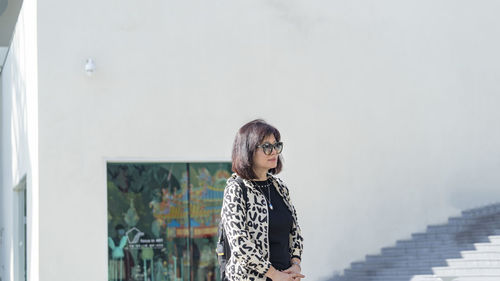 Woman looking away while standing against wall