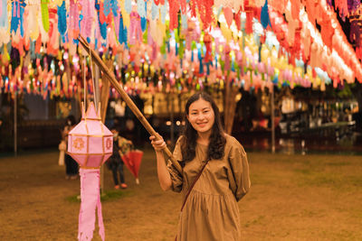 Asian woman holding paper lantern in annual lantern hanging tradition at night at temple, lamphun