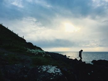 Silhouette man standing on cliff by sea against sky during sunset