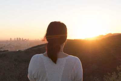 Rear view of woman looking at mountains against sky during sunset