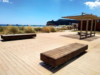 Empty benches on beach by building against sky