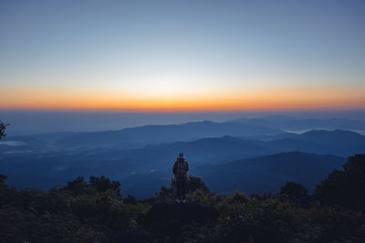 Rear view of silhouette man standing on mountain against sky at sunset