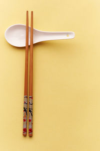 Directly above shot of chopsticks and spoon on yellow background