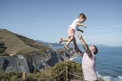 Father catching son at observation point against blue sky on sunny day