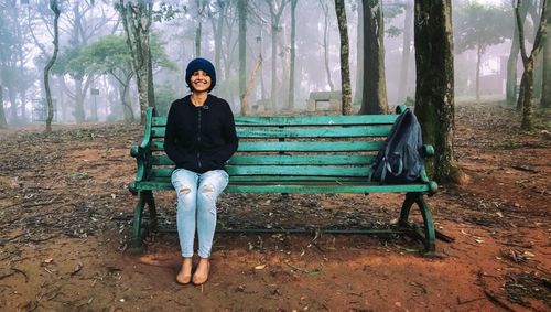 Full length portrait of young woman sitting on tree trunk in park